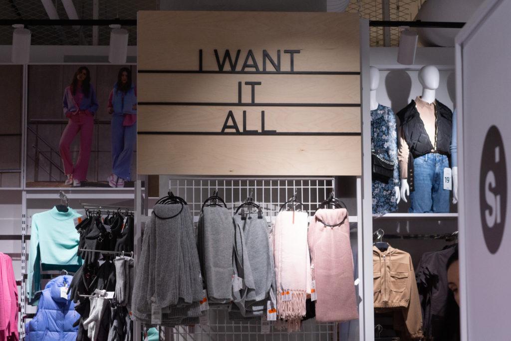 Kuva vaatekauoassa. Kuvassa vaatteita ja seinällä teksti "I want it all".