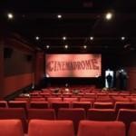Kuva melko tyhjästä elokuvateatterista. Punaiset penkit, hämärä valaistus. Valkokankaalla elokuvafestivaali Cinemadromen logo.